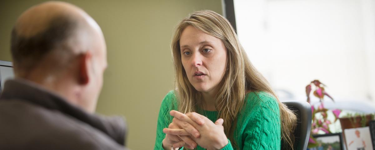 A picture of Amy, a white woman with blonde hair and a green shirt, one of PTLA's paralegals, meeting with a client, who has his back turned to the camera